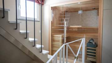 A modern interior with a staircase, a glass-enclosed sauna, and a wooden bench.