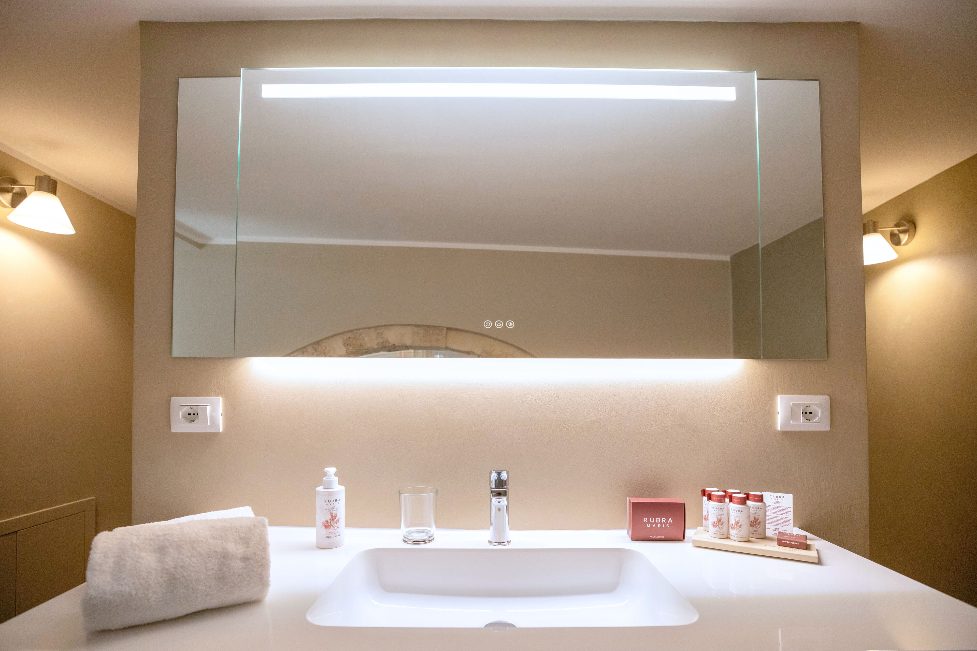 A bathroom with a large mirror, a sink, a towel, and toiletries.