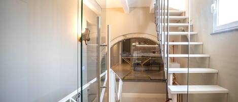 A modern interior with a glass partition, a staircase, and a dining area with a circular table.