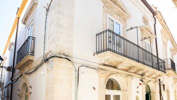 A historic building with a stone facade, arched doorways, and a balcony with a wrought iron railing.
