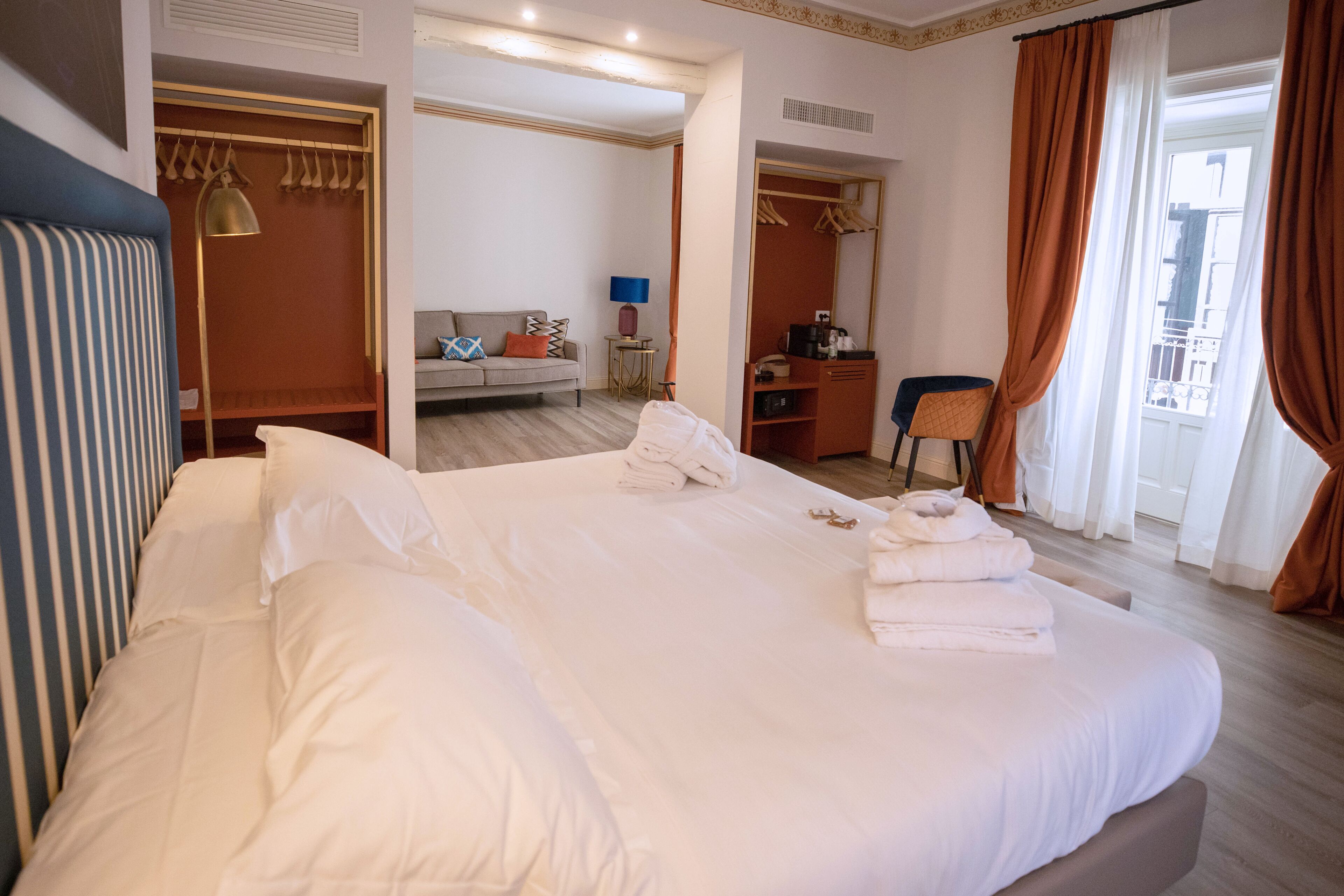 A hotel room with a large bed, a desk, a chair, a sofa, and a wardrobe.
