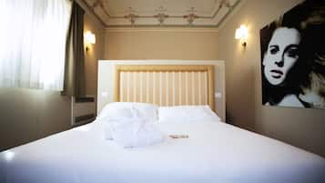 A hotel room with a large bed, white linens, a headboard, two wall sconces, and a large portrait on the wall.