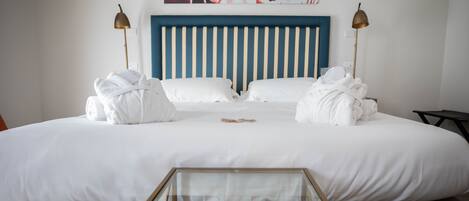 A neatly made bed with white linens and towels, a blue striped headboard, and two bedside lamps.