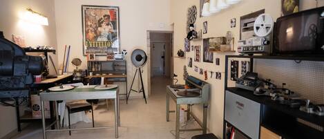 A compact studio apartment with a kitchenette, a dining area, and a living space with a television and various decorations.