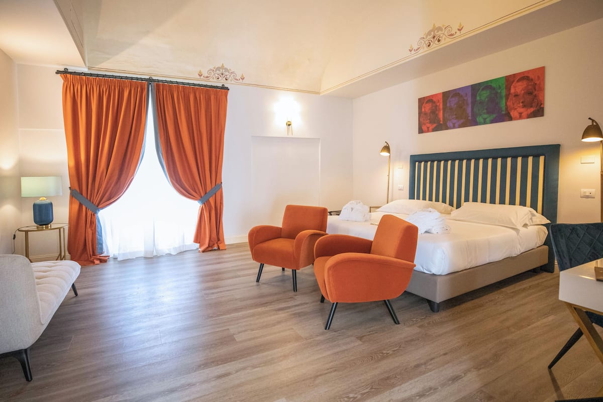 Et moderne hotelværelse med en seng, to orange lænestole, et skrivebord og et stort vindue med orange gardiner.