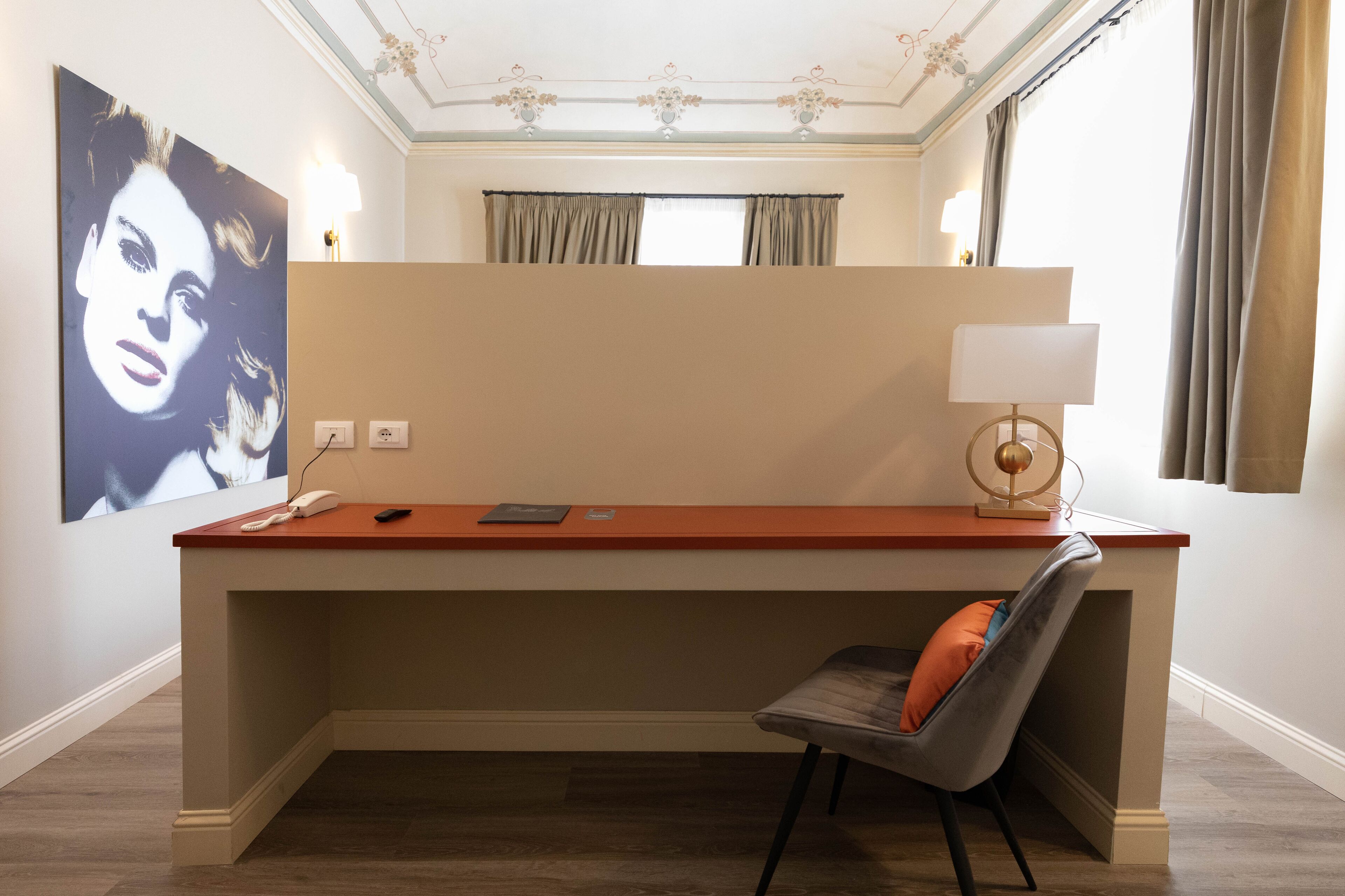 A hotel room with a desk, chair, and a large framed artwork on the wall.