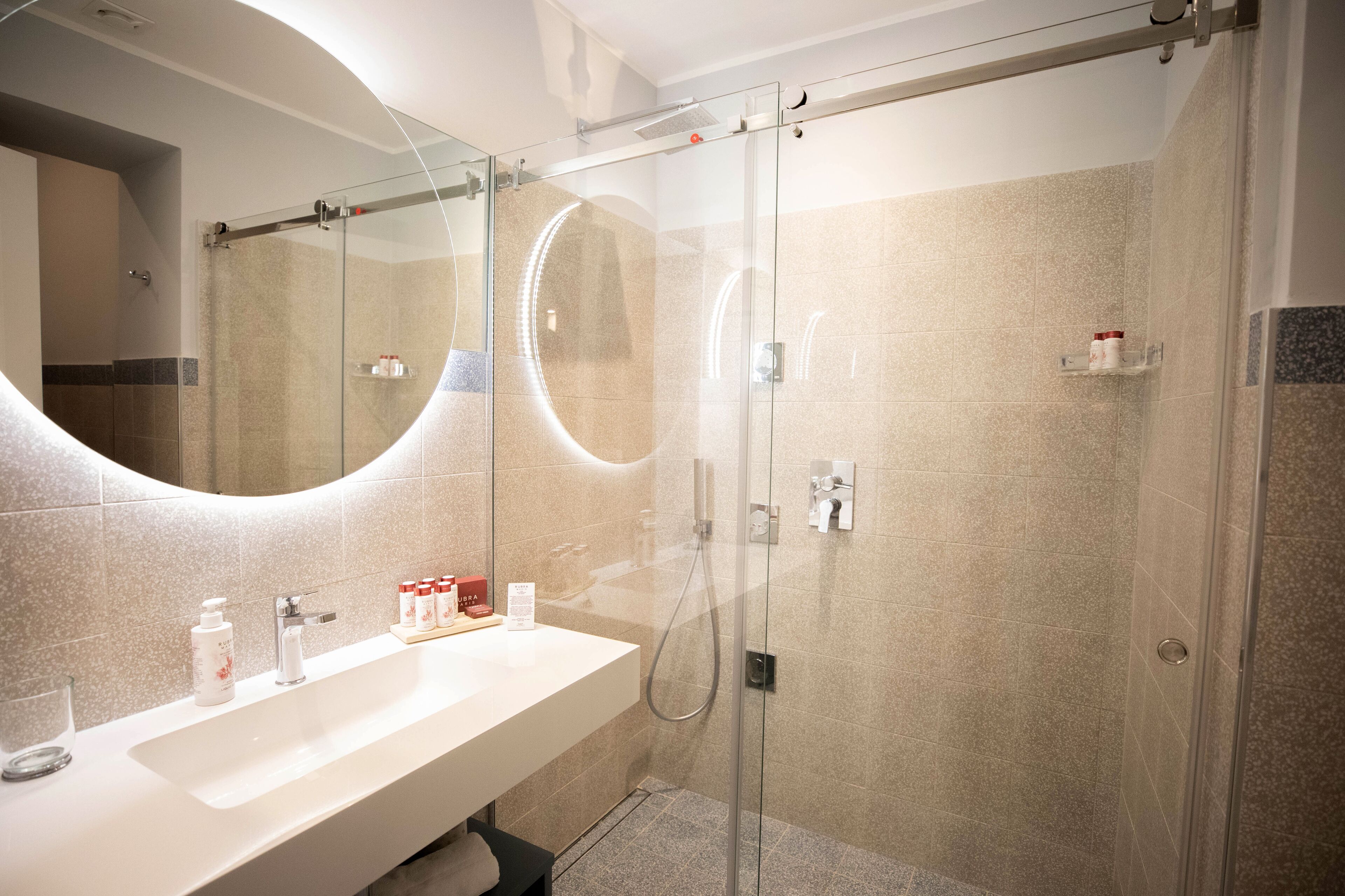 A modern bathroom with a glass-enclosed shower, a large mirror, and a white vanity with toiletries.