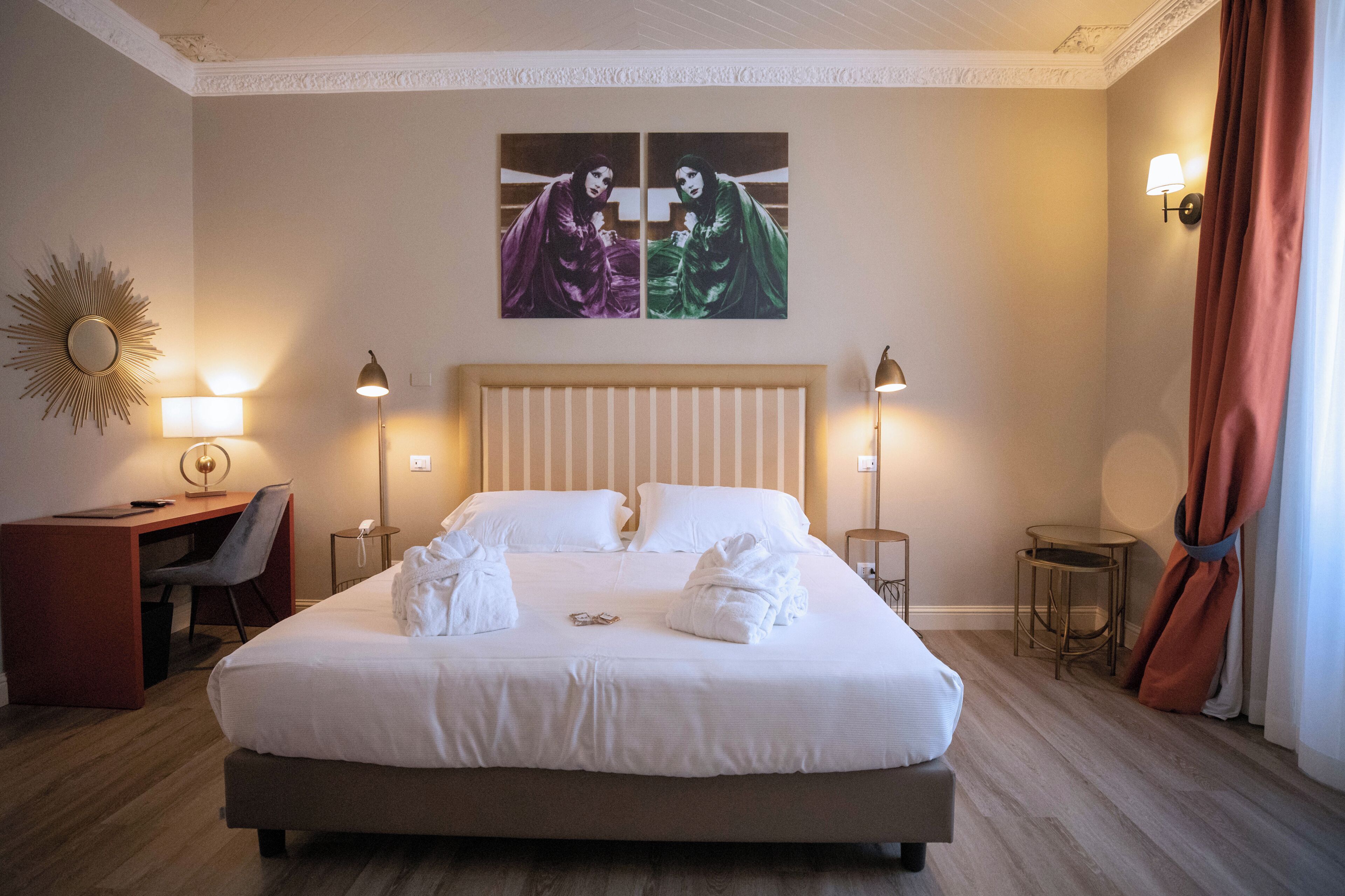 A hotel room with a large bed, bedside lamps, a desk with a chair, and a mirror.