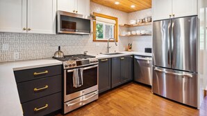 Una cocina moderna con armarios blancos, electrodomésticos de acero inoxidable y techo de madera.