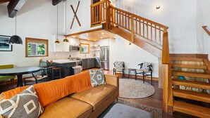 Una cocina moderna con una isla central, una escalera de madera y una zona de estar acogedora con sofá y reposapiés.