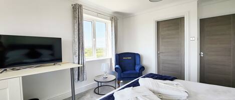 A hotel room with a bed, a desk with a TV, a chair, and a door.