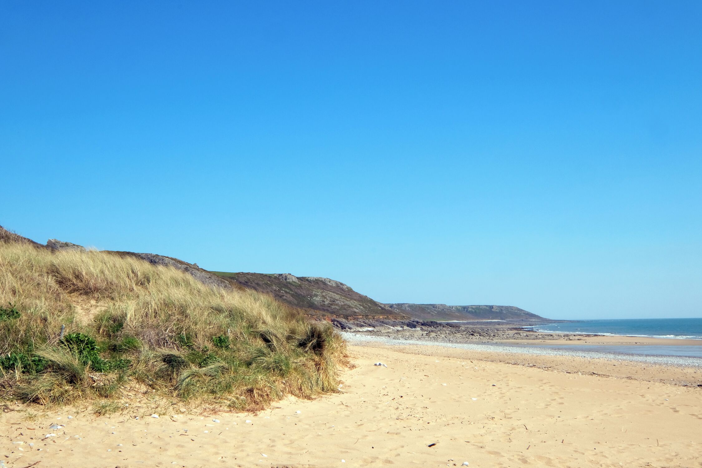 A sandy beach with dunes and a clear blue sky.