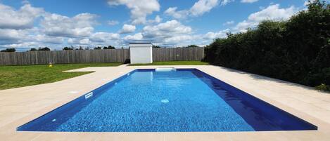 A rectangular swimming pool with a tiled deck surrounding it.