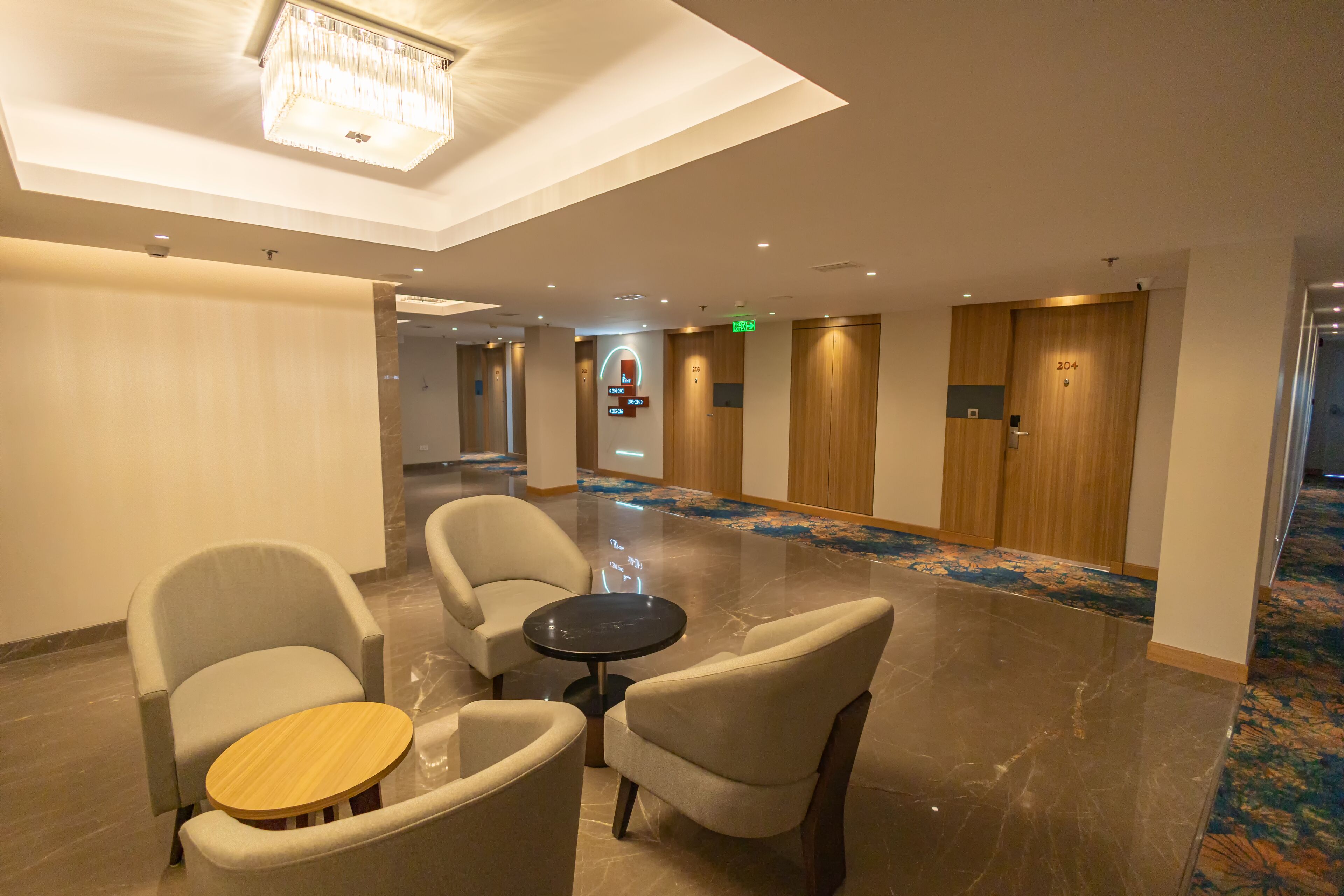 A hotel lobby with a chandelier, seating area with chairs and a small table, and a carpeted floor.