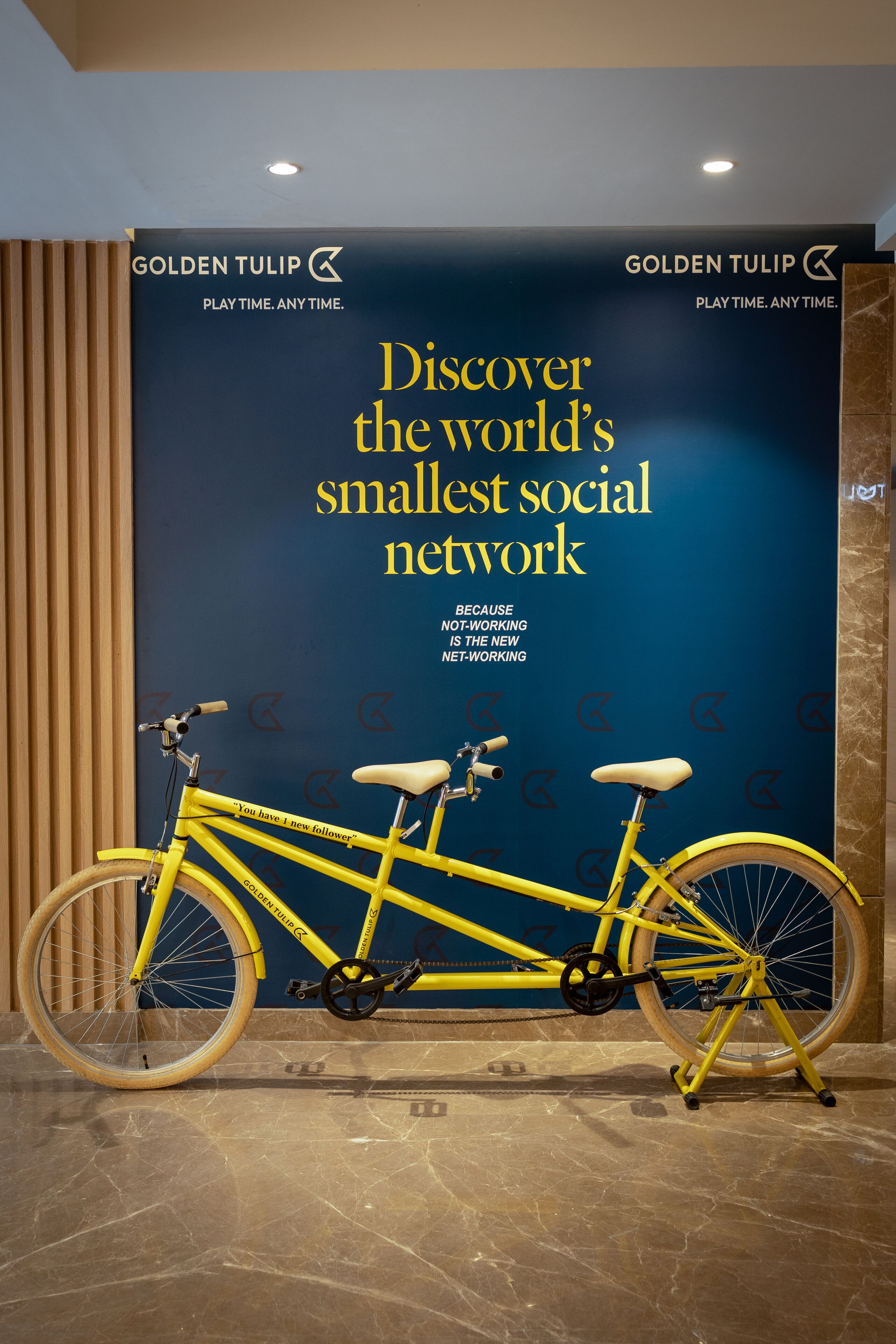 A yellow bicycle in front of a wall with a Golden Tulip advertisement.