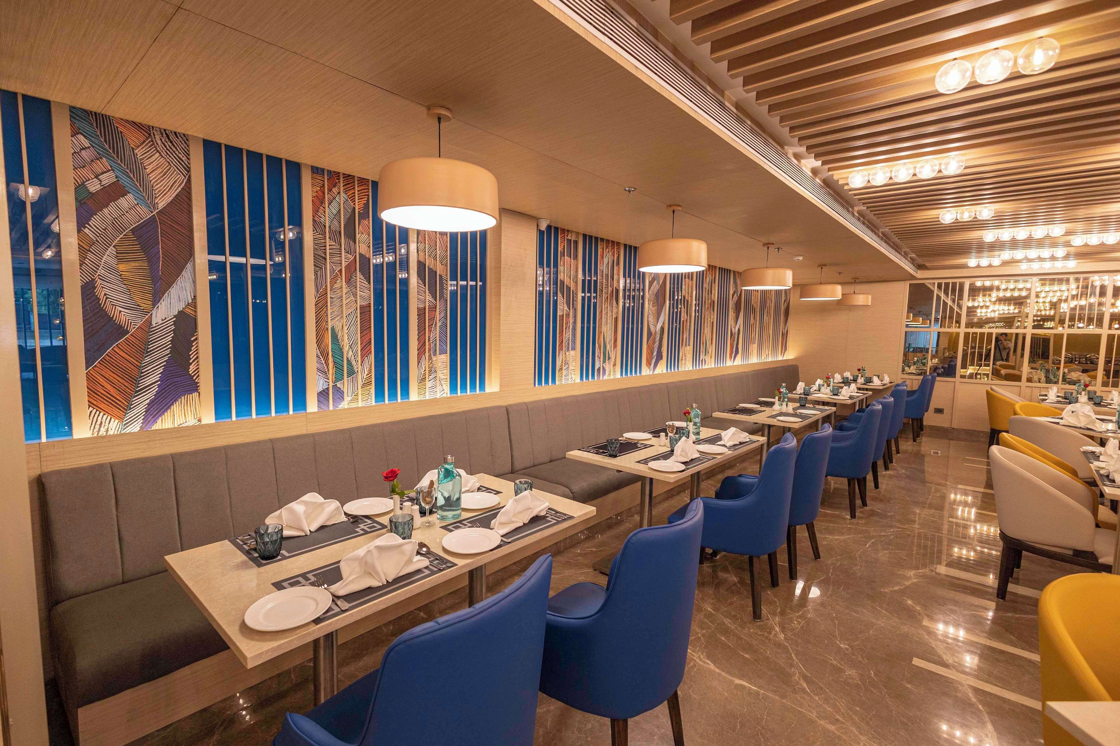 A restaurant with long tables, blue chairs, and a decorative wall with vertical patterns.