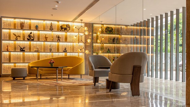 A modern lobby with a reflective floor, a sofa, a chair, and a wall with decorative items. - Golden Tulip Bhopal (Bhopal)