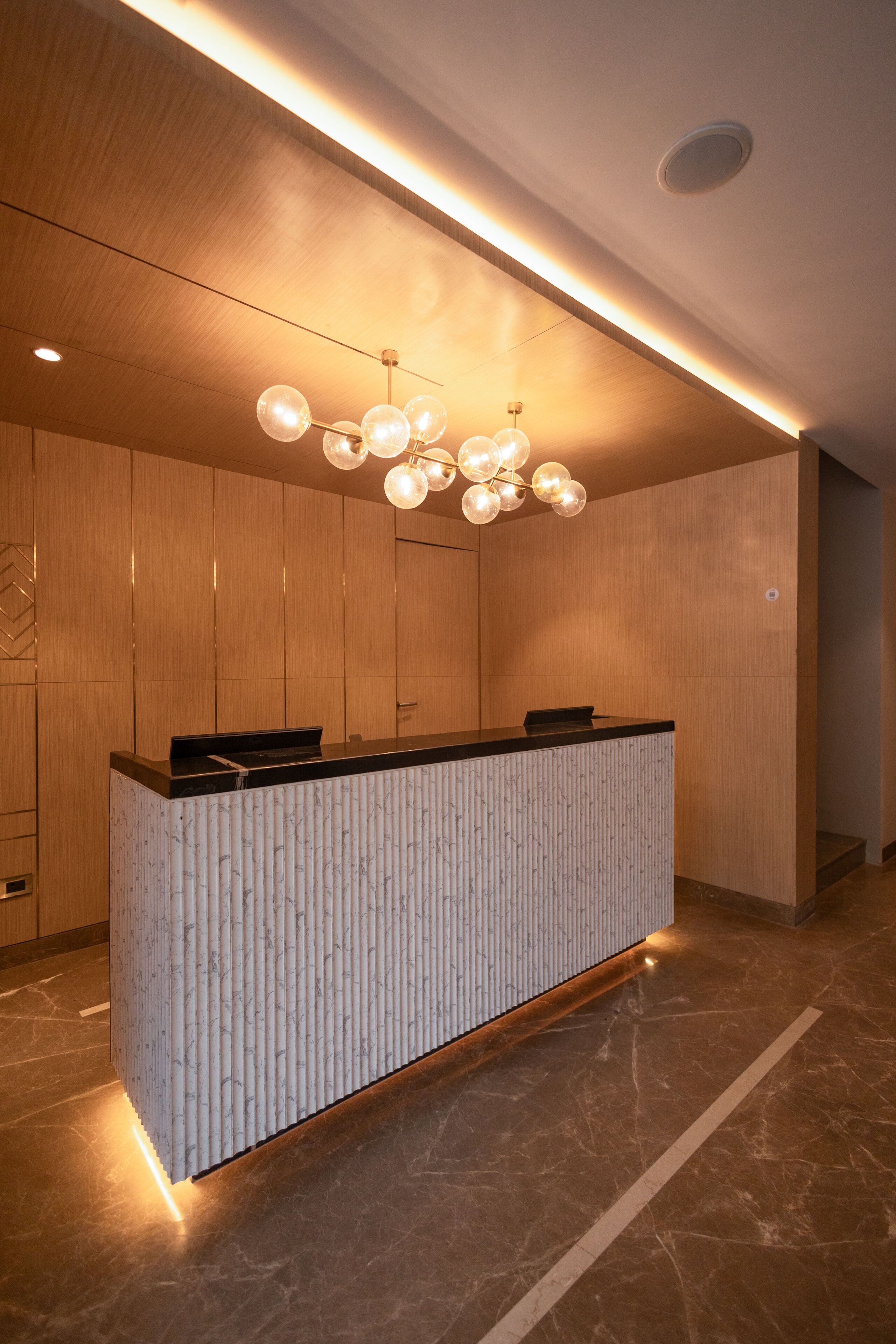 A reception desk with a modern design, a wooden wall, and a ceiling light fixture.