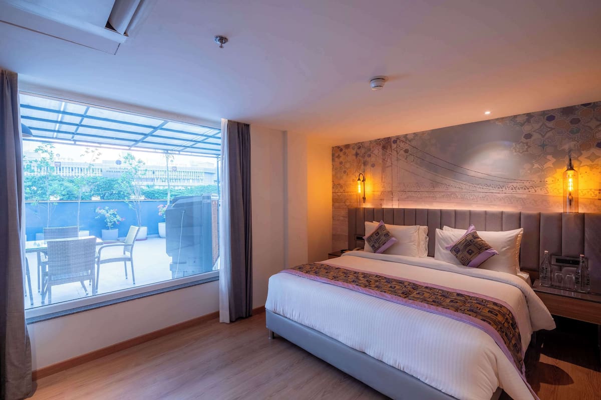 Une chambre d’hôtel avec un grand lit, une vue sur l’extérieur, un mur décoré d’un motif et une table de chevet avec une lampe.
