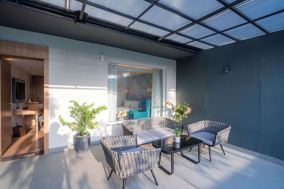 Un espace extérieur moderne aménagé avec des meubles en osier et des plantes en pot, une porte vitrée donnant sur une pièce, et une vue sur le paysage urbain par la fenêtre.