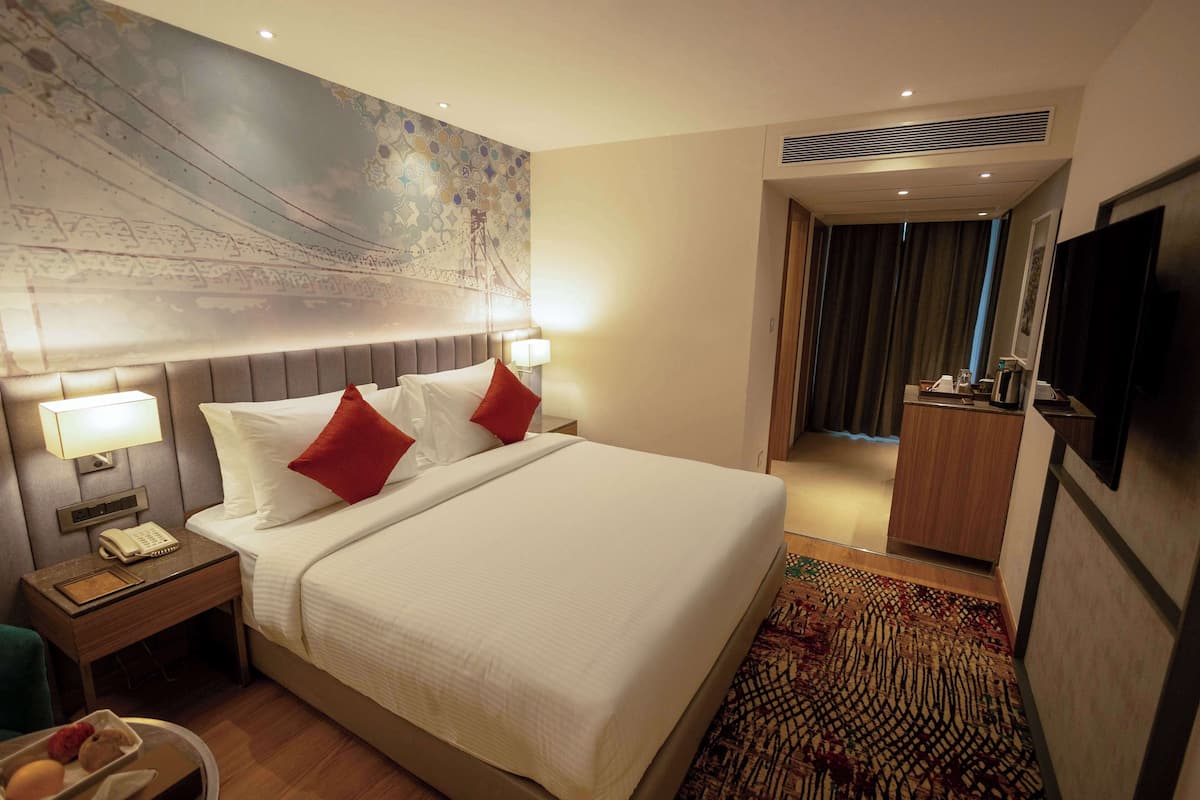 Une chambre d’hôtel avec un grand lit, deux lampes de chevet, un téléphone, une petite table et un mur orné d’un grand tableau abstrait.