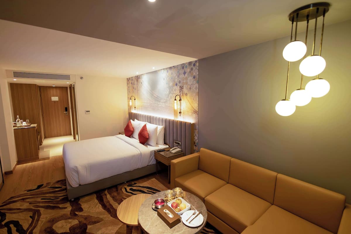 Une chambre d’hôtel comprenant un lit, un canapé, une petite table ronde servant de table basse, ainsi que des accessoires, une table de chevet et un luminaire fixé au mur.
