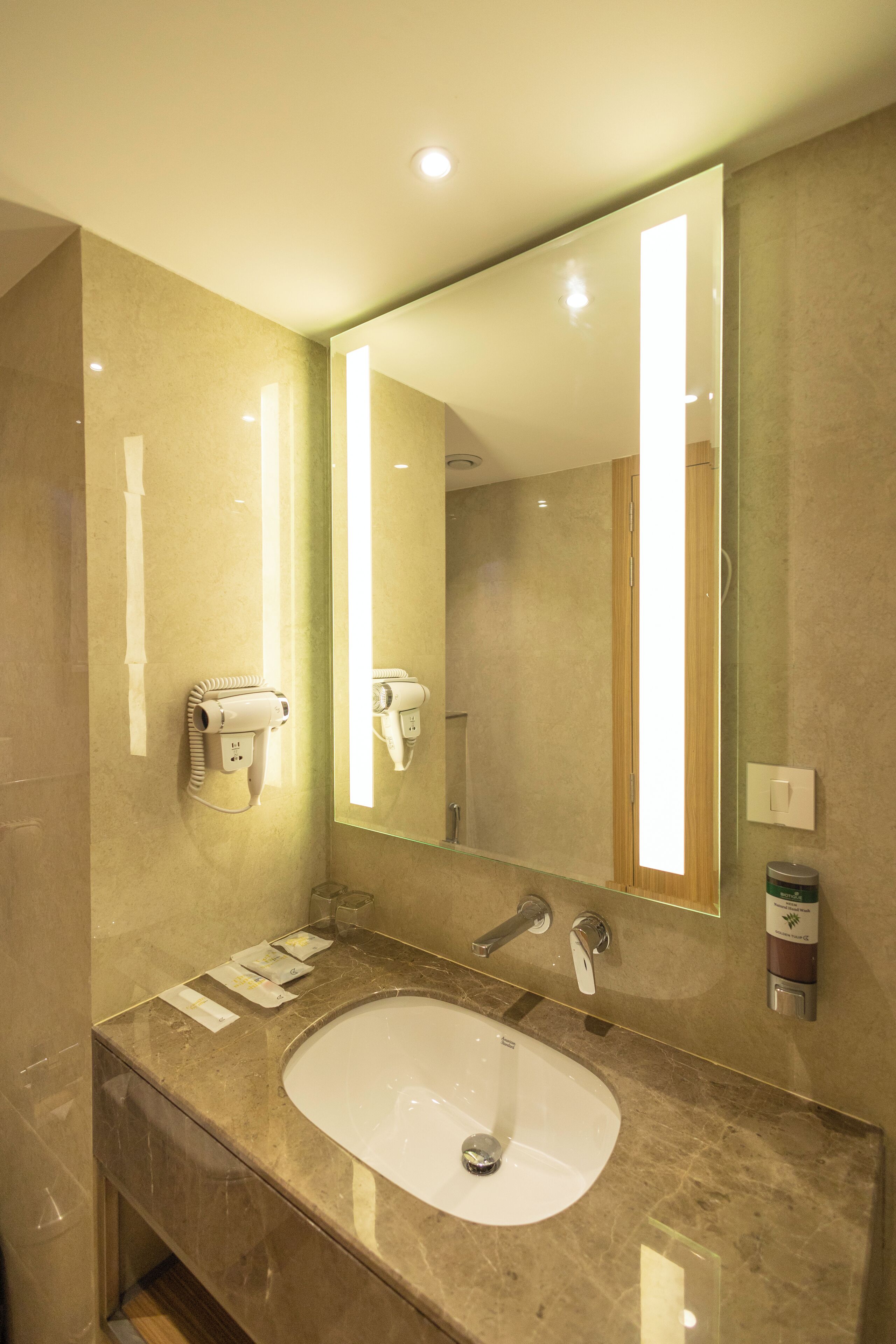 Een moderne badkamer met een grote spiegel, een wastafel, een haardroger en een zeepdispenser.