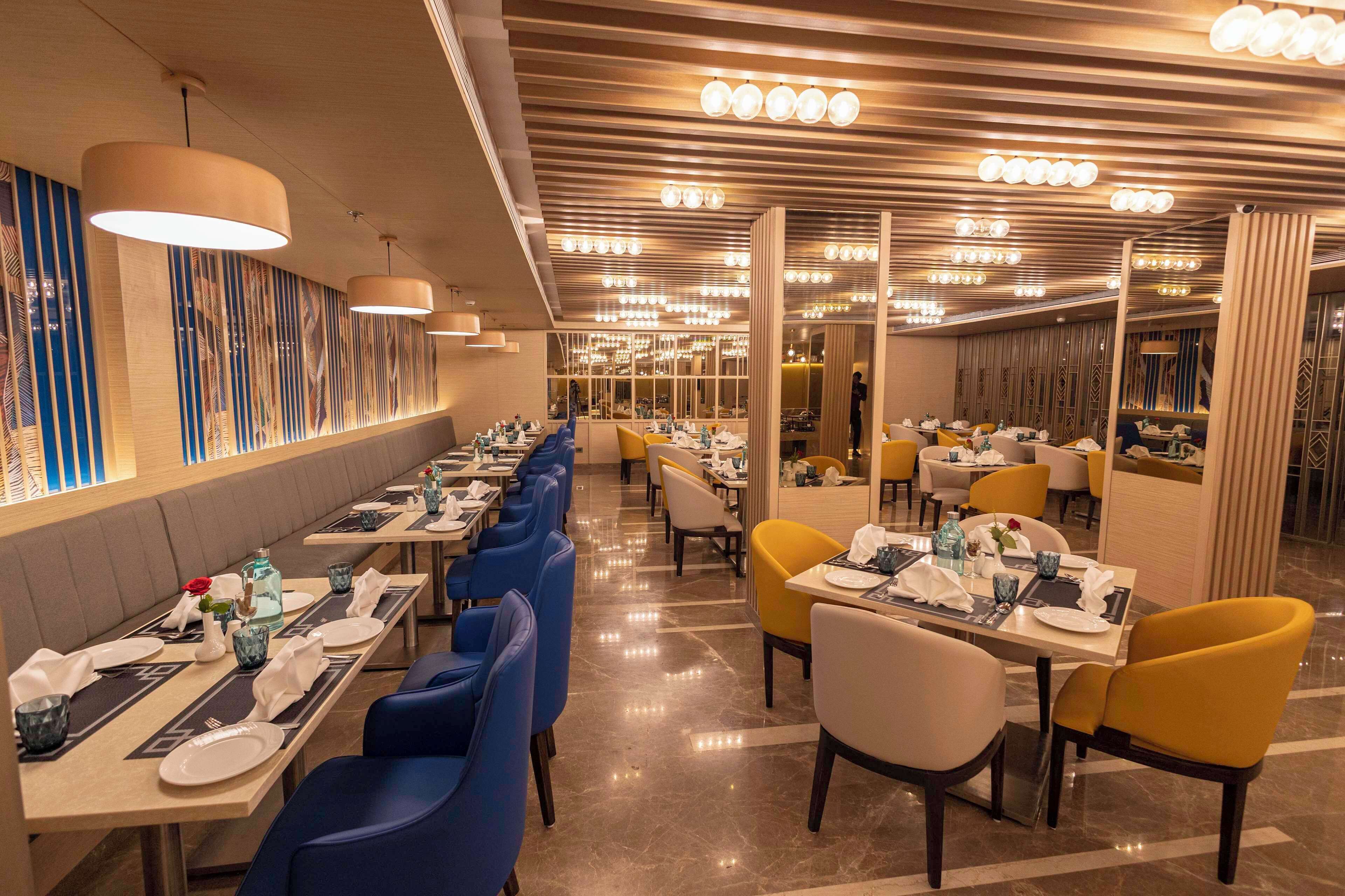 Ein geräumiges Restaurant mit langen Tischen, blau-gelben Stühlen und einem modernen Deckengestaltung.
