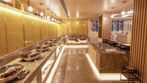 A buffet area with a long counter, multiple serving stations, and a seating area with tables and chairs. - Golden Tulip Bhopal (Bhopal)