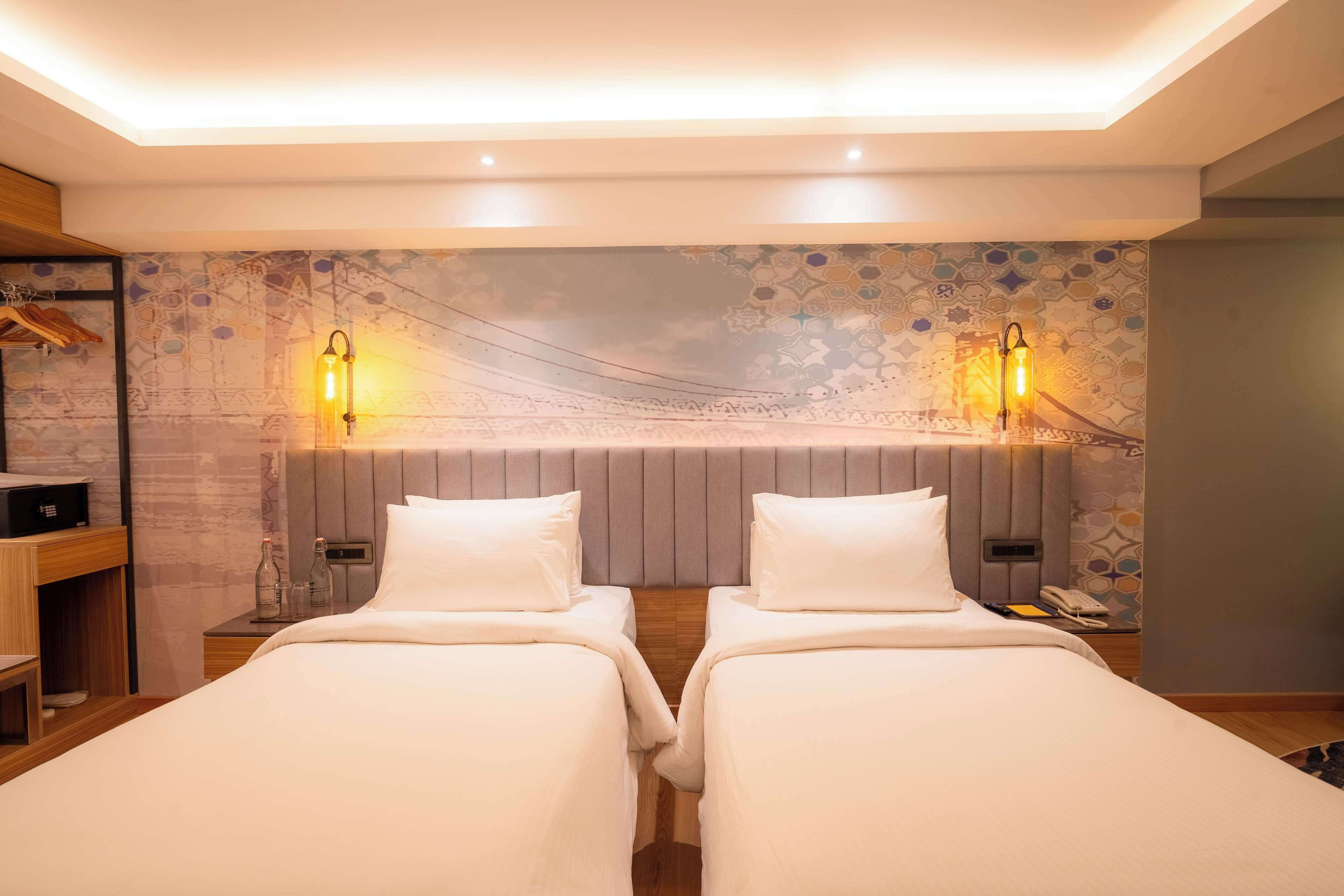 Una habitación de hotel con dos camas, una mesita de noche de madera, una pared con diseño geométrico y dos lámparas de pared.