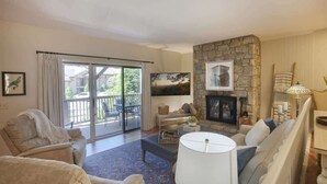 A spacious living room with a stone fireplace, comfortable seating, and a large sliding glass door leading to a balcony. - Chetola Resort, Pine #3, in Blowing Rock (Blowing Rock)