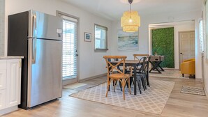 A modern kitchen with a stainless steel refrigerator, wooden dining table, and chairs. There is a patterned rug on the floor, and a green wall in the background. - Blue Bungalow w/ Free Golf Cart (Covington)