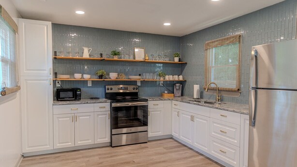 A modern kitchen with white cabinets, stainless steel appliances, and a blue tiled backsplash. - Blue Bungalow w/ Free Golf Cart (Covington)