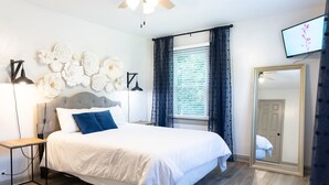 A bedroom with a bed, a nightstand, a mirror, and a wall with floral decorations. - Blue Bungalow w/ Free Golf Cart (Covington)
