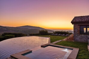 Zona de piscina con una estructura de piedra y vista a colinas distantes al atardecer.