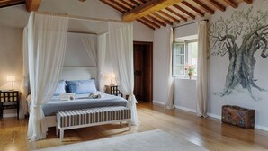 Un dormitorio con cama con dosel, techo de madera, un gran mural de un árbol y una maleta en el suelo.