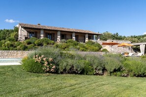 Un bâtiment en pierre avec un toit en tuiles, une piscine et une végétation luxuriante.