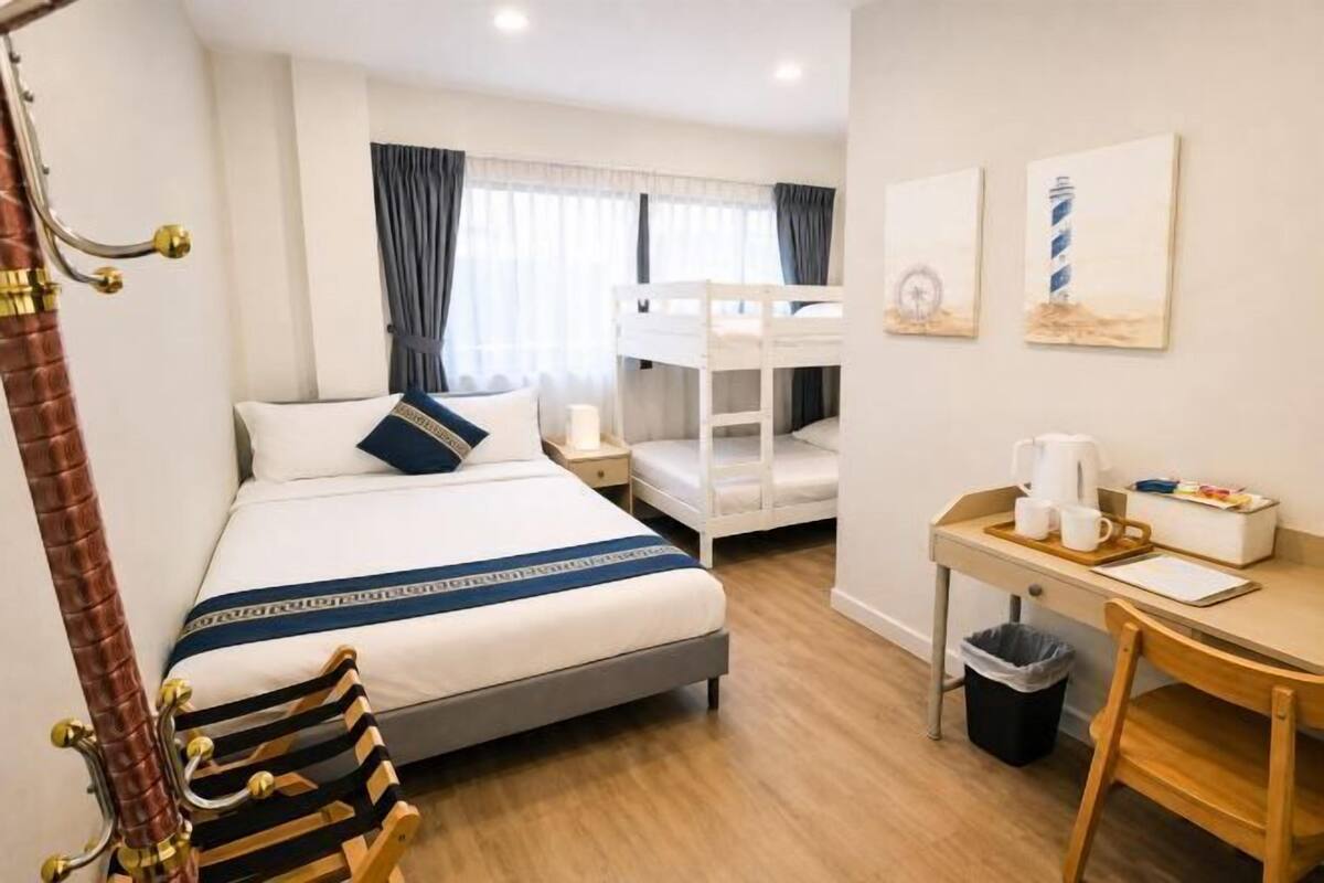 A hotel room with a bed, bunk beds, a desk with a chair, a trash bin, and artwork on the walls.