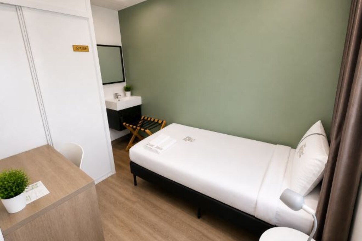 A small, modern room with a bed, a desk, a chair, and a small plant.