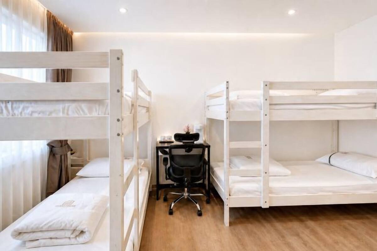 A bunk room with three bunk beds, a desk with a chair, and a window with curtains.