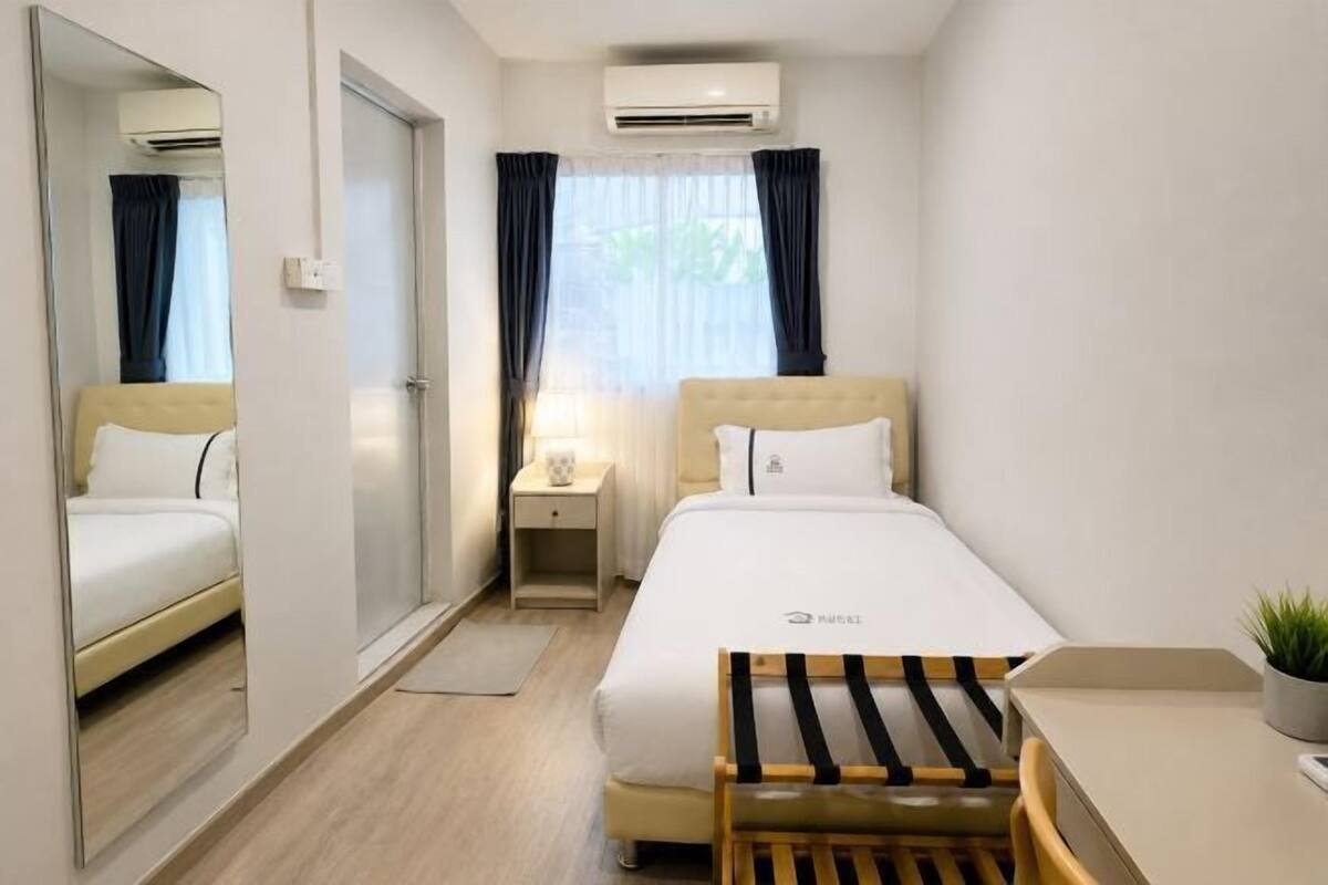 A hotel room with a bed, bedside table, mirror, and an air conditioning unit.