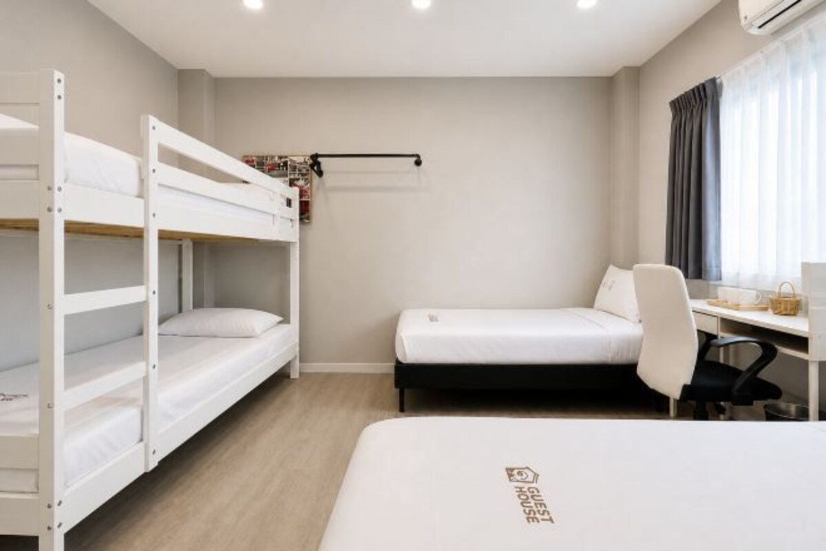 Una habitació amb lliteres, un escriptori, una cadira, un llit i una finestra amb cortines.