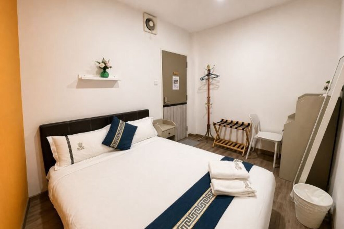 A hotel room with a bed, a small table, a chair, a coat rack, and a mirror.