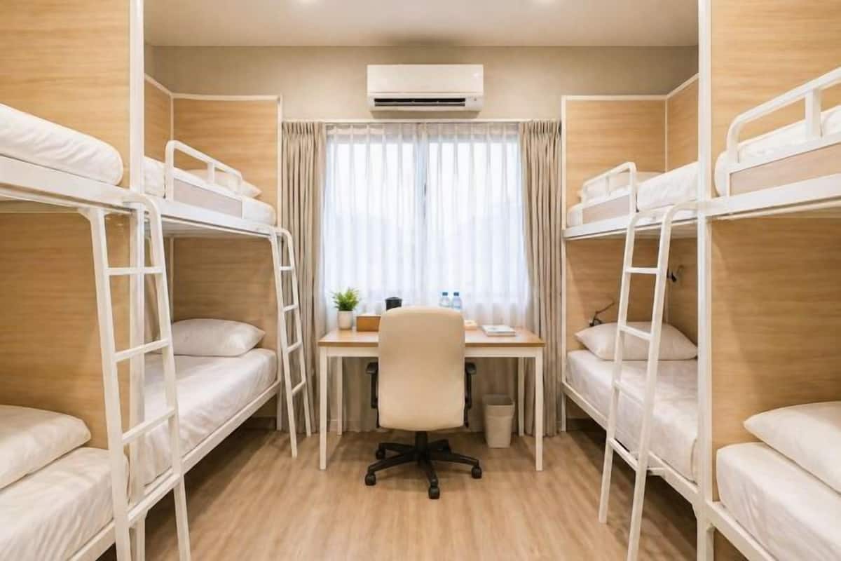 A room with bunk beds, a desk, a chair, an air conditioner, and a window with curtains.