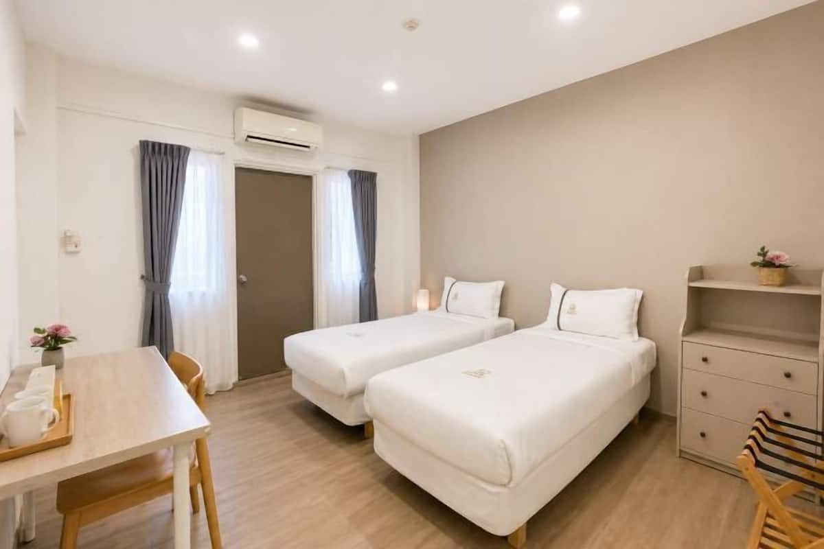 A hotel room with two beds, a desk with a chair, a small table with a tray, and a shelf with a vase.