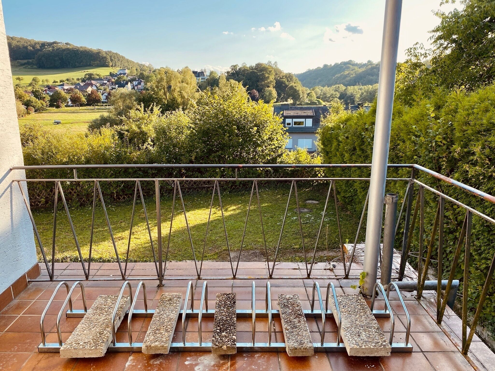 Ein Balkon mit Blick auf eine grüne Landschaft und ein Haus in der Ferne.
