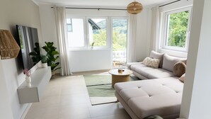 A modern living room with a sofa, a coffee table, and a large window offering a view of greenery.
