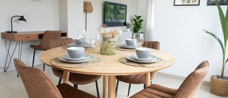 Un comedor con una mesa redonda de madera, sillas tapizadas en tono marrón y un jarrón decorativo en el centro.