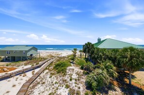A beachside property with a wooden boardwalk, a green-roofed building, and a view of the ocean.