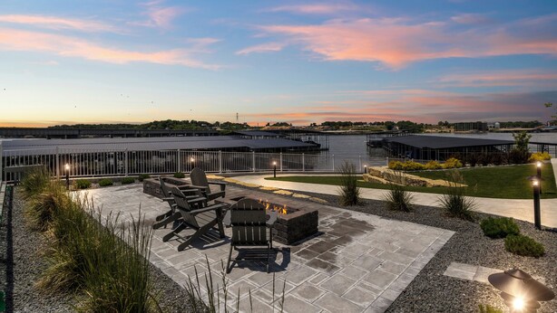An outdoor patio area with seating and a fire pit, surrounded by a landscaped garden and a view of a body of water. - Topsider Experience in the Heart of Osage Beach (Osage Beach)